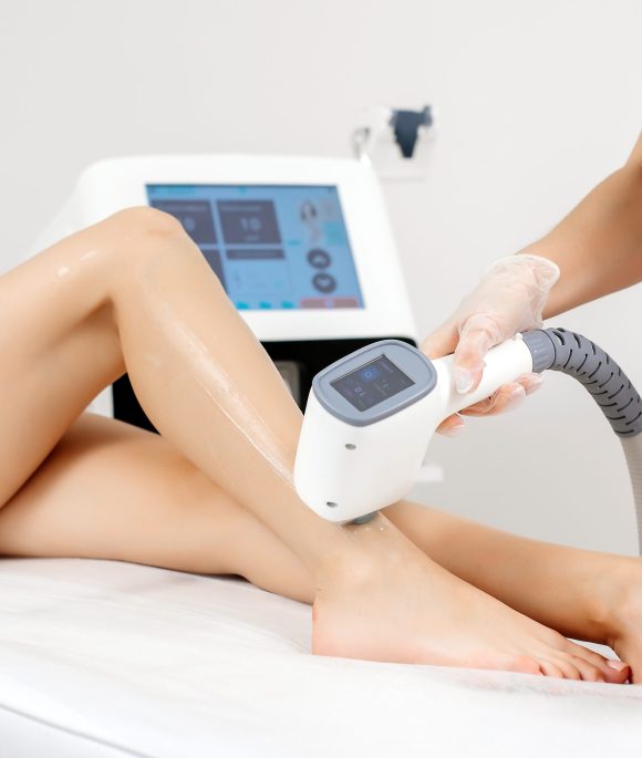 A female cosmetologist does laser hair removal on the slender legs of a beautiful young woman lying on a medical couch in a beauty salon. Cosmetology, hair removal and spa concept. Body care. Close-up